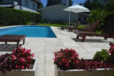 a swimming pool with benches and flowers and an umbrella at Casa Simona Villa General Belgrano in Villa General Belgrano