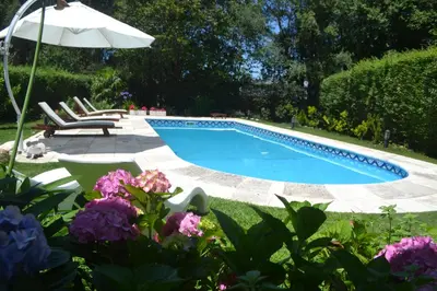 a swimming pool with chairs and an umbrella and some flowers at Casa Simona Villa General Belgrano in Villa General Belgrano