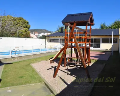 a wooden play structure in front of a pool at Duplex del Sol in Villa Carlos Paz