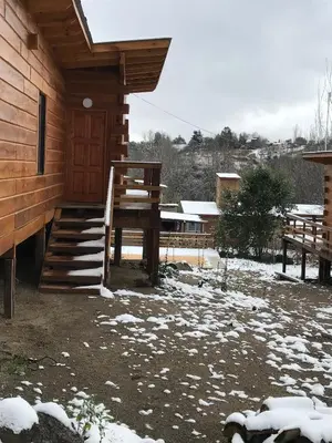 a cabin with snow on the ground next to a porch at Cabañas San Urbano 1 in Villa Yacanto