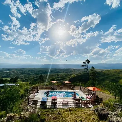 a swimming pool on top of a hill with the sun in the sky at Cabañas PAIGÜEN in Villa Yacanto