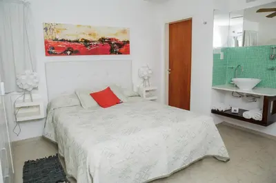 a white bedroom with a bed with a red pillow at Complejo Turístico Las Catalpas in Mina Clavero