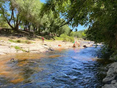 a river with people standing on the bank of it at Departamentos LOS CEDROS in Mina Clavero