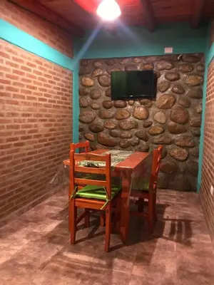 a table with two chairs and a tv on a stone wall at Departamentos la Familia NONO in Nono