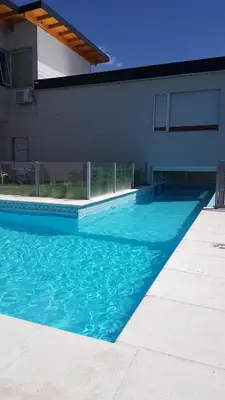 a blue swimming pool next to a house at Alamo Hotel in Villa Carlos Paz