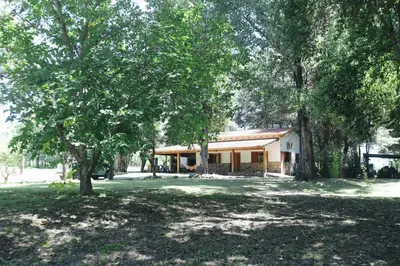 a house with trees in front of a yard at Cabaña Modestita - FINCA PUDUAM in Villa General Belgrano