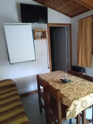 a dining room table and chairs with a white board on the wall at Cabañas La Pirca in Santa Rosa de Calamuchita