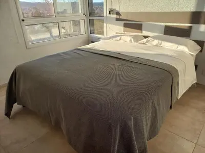 a bed in a bedroom with two windows at Luces Casas de Montaña in Villa del Dique
