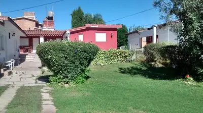 a yard with a red house and some bushes at Amanitas Posada in Villa Carlos Paz