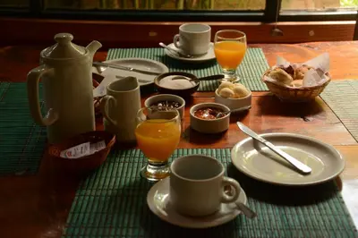 a table with cups and plates of food and orange juice at Manantial Hostería & Cabañas in Nono