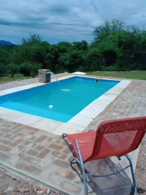 a red chair sitting next to a blue swimming pool at Cabañas Guayacán in Bialet Massé