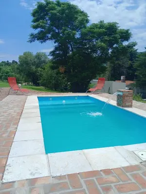 a blue swimming pool with two chairs and a tree at Cabañas Guayacán in Bialet Massé
