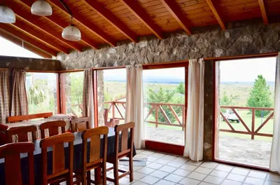 a dining room with a table and chairs and windows at Cabaña julian in La Cumbrecita