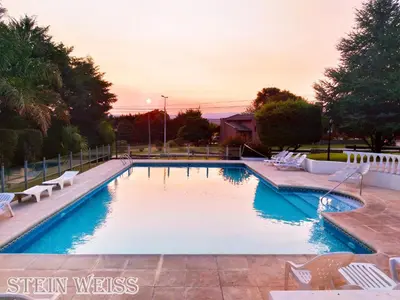 a swimming pool with white chairs and a sunset at Cabañas Stein Weiss in Santa Rosa de Calamuchita