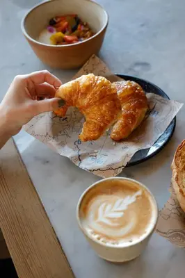 a person holding a piece of food and a cup of coffee at MAE Singular Hotel in Cordoba