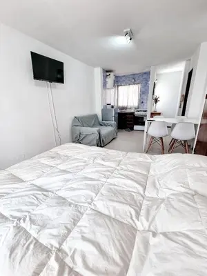 a bedroom with a white bed and a living room at DPTO 1 CUADRA SANATORIO ALLENDE in Cordoba