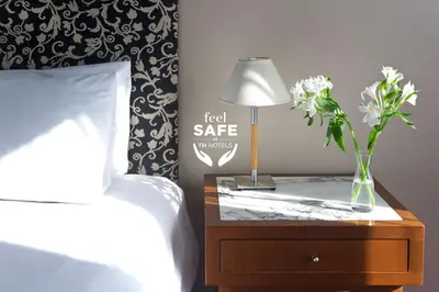 a bedroom with a bed and a table with a lamp and flowers at NH Córdoba Panorama in Cordoba