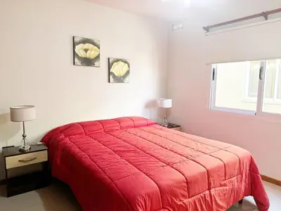 a red bed in a white room with a window at Departamentos Miralejos 6 in Villa Carlos Paz