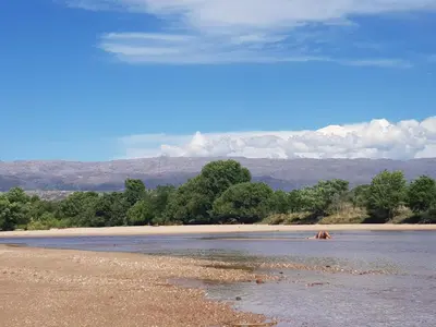 a body of water with trees and a beach at Favre Suites in Mina Clavero