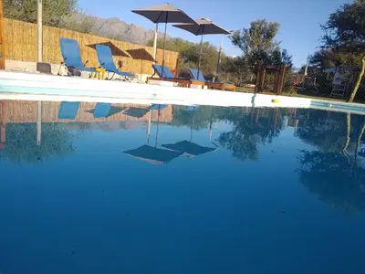 a swimming pool with blue chairs and an umbrella at Cabañas Tierra del Sol in Las Rabonas