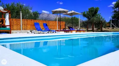 a swimming pool with blue chairs and umbrellas at Cabañas Tierra del Sol in Las Rabonas