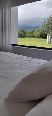 a bed with a pillow in front of a window at El Campo Departamentos in Merlo
