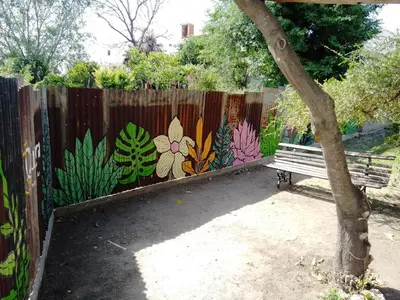 a wooden fence with a bench in front of a fence with a flower mural at Complejo Quiya - Departamento Los Espinillos con hidromasaje in Alta Gracia