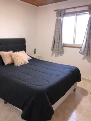 a bedroom with a large bed with blue sheets and a window at CABAÑAS FENIX con EL ARROYO AMBOY RODEANDO LA PROPIEDAD reservar con 24 hs de anticipación in Villa Amancay