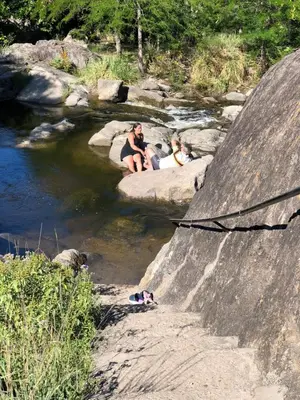 a group of people sitting on rocks in a river at CABAÑAS FENIX con EL ARROYO AMBOY RODEANDO LA PROPIEDAD reservar con 24 hs de anticipación in Villa Amancay