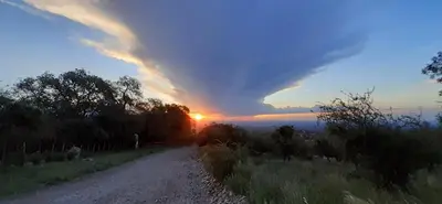 a storm cloud over a dirt road at sunset at COSTA COM Cabañas in Merlo