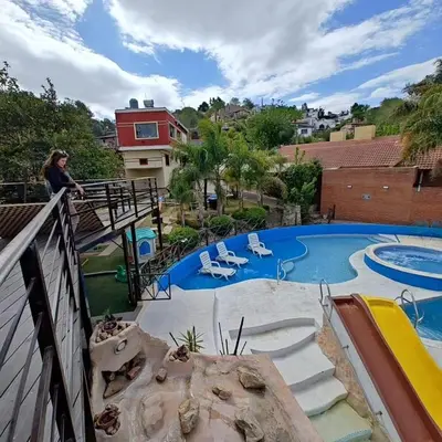 a woman standing on a balcony next to a swimming pool at Complejo Los Cipreses in Villa Carlos Paz