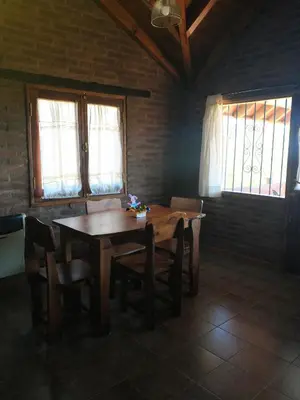 a wooden table and chairs in a room with windows at Cabañas Stone Hill in Santa Rosa de Calamuchita