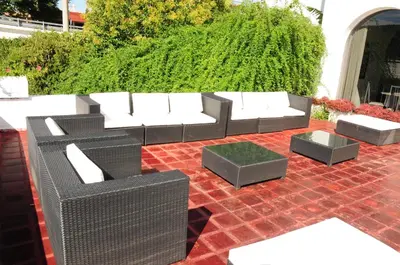 a patio with a couch and tables and a hedge at Hostal de la Costa in Villa Carlos Paz