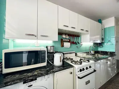 a white kitchen with a microwave and a stove at Amplio Piso Vintage, Terraza con Vista a Sierras in Cordoba