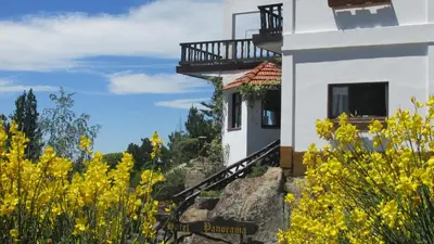 a white building with a balcony in a field of yellow flowers at Hotel Panorama in La Cumbrecita