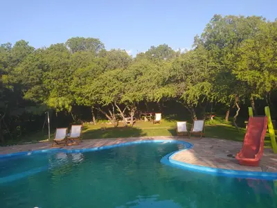 a swimming pool with a slide and chairs and trees at Las Casitas, cabañas & suites in Pincén