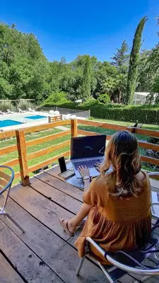 a woman sitting in a chair with a laptop on a deck at Atelier Hotel de Charme in Villa General Belgrano