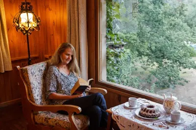 a woman sitting in a chair reading a book by a window at Hotel Las Cascadas in La Cumbrecita