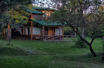 a wooden house with a green roof in a field at Cabañas Cuatro Horizontes in Villa General Belgrano
