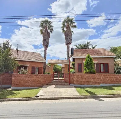 a house with two palm trees behind a brick fence at La Margarita Lofts - Solo 2 Adultos in Mina Clavero