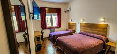 a bedroom with two beds and a table and windows at Grand Hotel Rio Cuarto in Río Cuarto