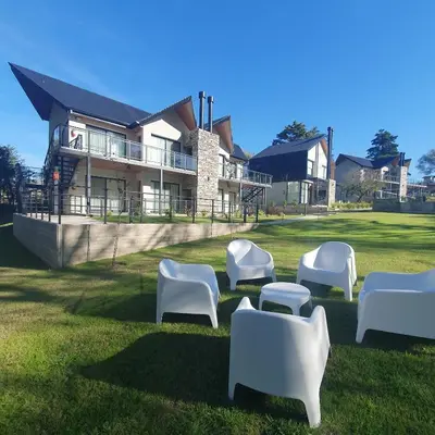 a group of white chairs sitting in the grass in front of a house at El Nogal Apart Hotel in Villa General Belgrano