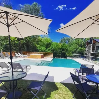 a pool with tables and chairs and an umbrella at El Nogal Apart Hotel in Villa General Belgrano