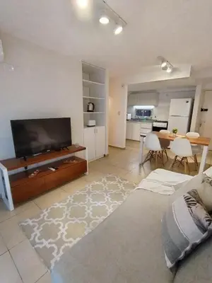 a living room with a flat screen tv and a kitchen at Departamento Boho Chic Corazón de Nueva Córdoba in Cordoba