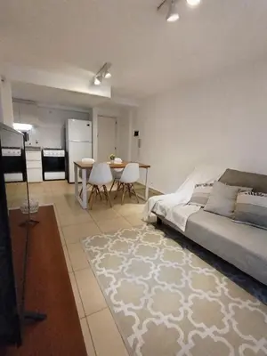 a bedroom with a bed and a table and a kitchen at Departamento Boho Chic Corazón de Nueva Córdoba in Cordoba