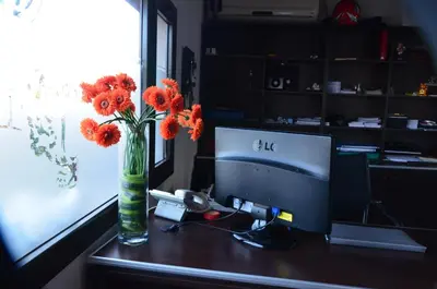a desk with a computer and a vase with orange flowers at Posada Loma del Tigre in Los Reartes