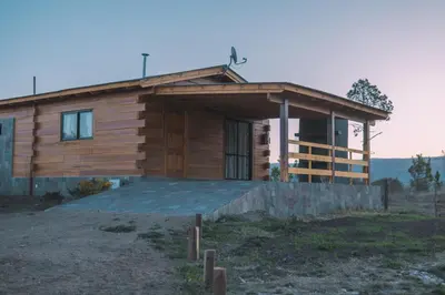 a wooden house with a large porch in a field at Complejo Anthea in Villa Yacanto