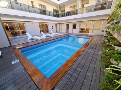 a swimming pool with a wooden deck and a building at Dpto Nva Cba, pileta seguridad, cochera in Cordoba