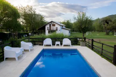 a swimming pool with white chairs and a house at Cabañas Los 2 Algarrobos in Santa Rosa de Calamuchita