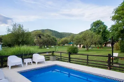 a swimming pool with white chairs and a fence and mountains at Cabañas Los 2 Algarrobos in Santa Rosa de Calamuchita